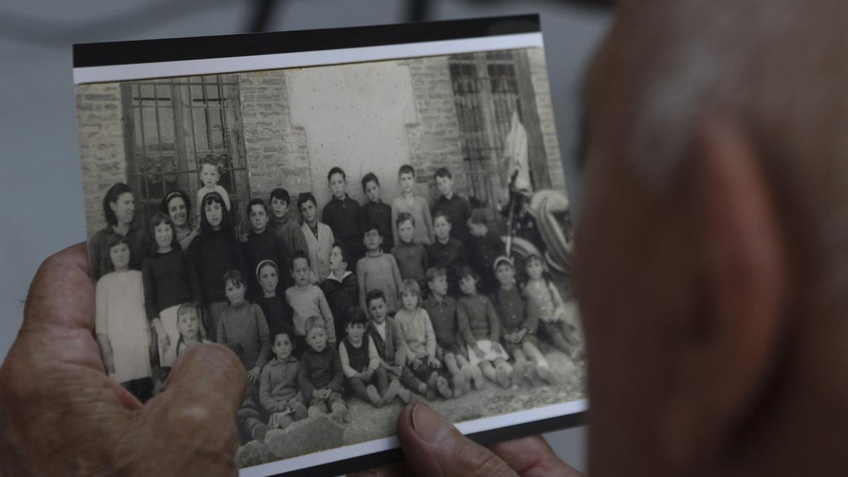 UN HOMBRE SOSTIENE UNA FOTOGRAFIA ANTIGUA DE LA MAESTRA Y LOS NIÑOS DEL COLEGIO