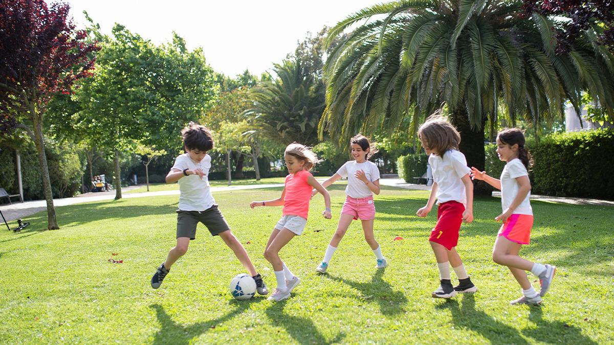 Un grupo de niños y niñas juegan al fútbol en un parque