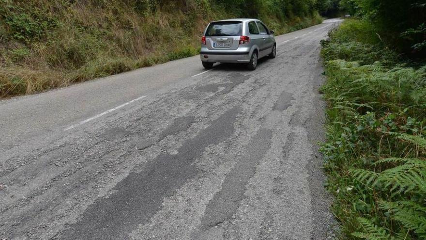 Un vehículo circula por un tramo deteriorado de la carretera AS-117.