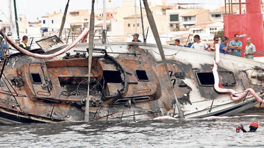 El velero incendiado en Portocolom es izado por una grúa, ante la mirada de los agentes y especialistas.