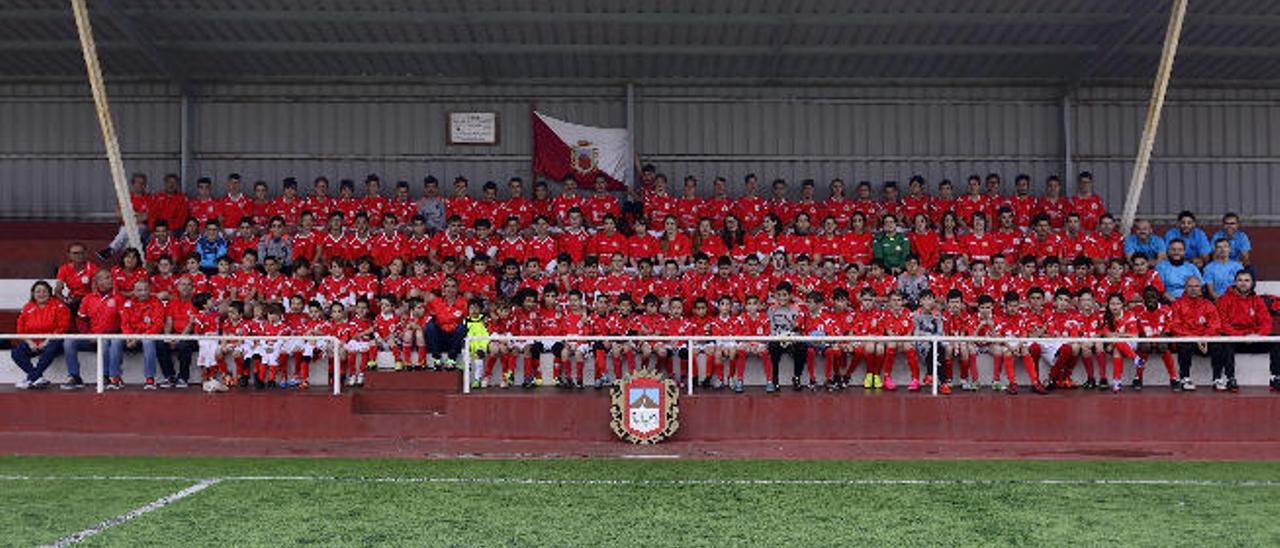 Foto de familia con todos los equipos que forman la cadena del CD Firgas, con sus respectivos técnicos, en la grada del campo Domingo Ponce.