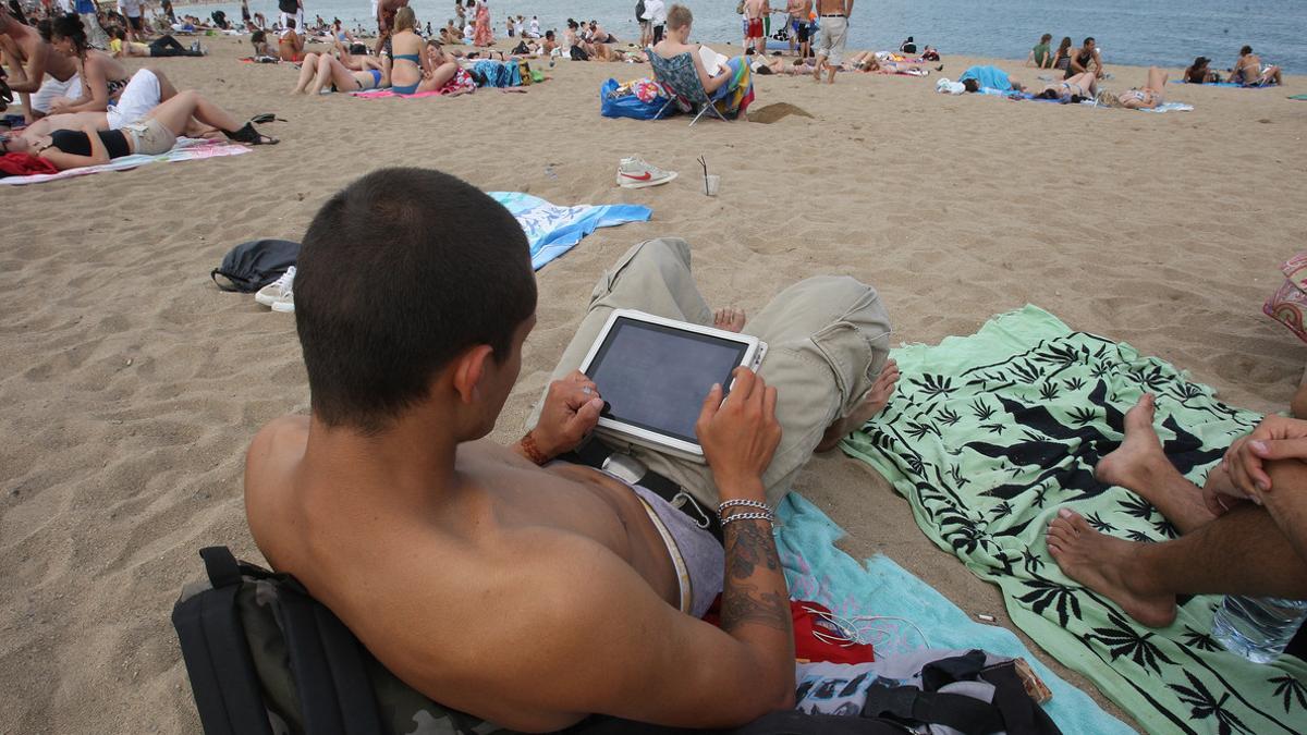 Un joven, con una tablet en la playa de la Barceloneta, en julio.