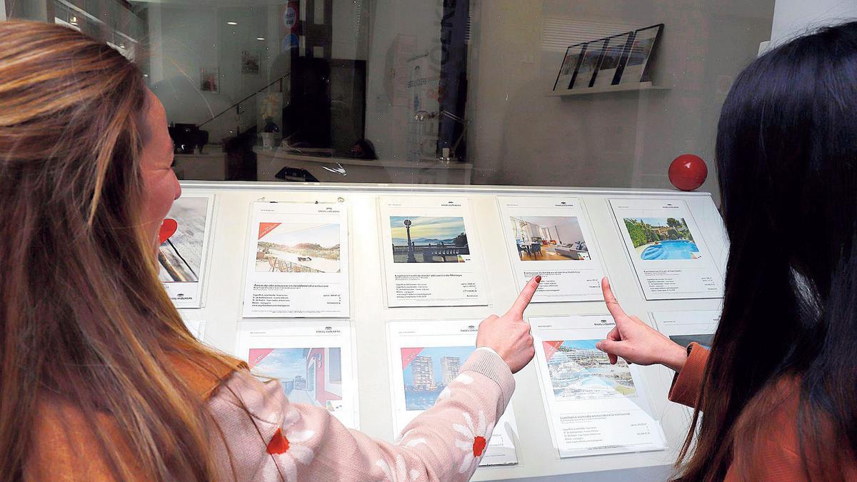 Dos jóvenes miran ofertas de viviendas en una inmobiliaria en Málaga.