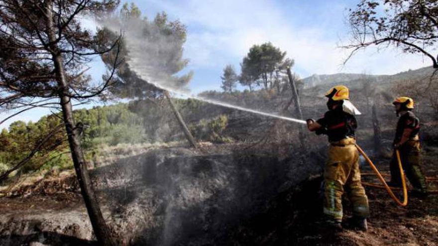 Dos bomberos refrescan parte de la superficie forestal que fue calcinada por las llamas.