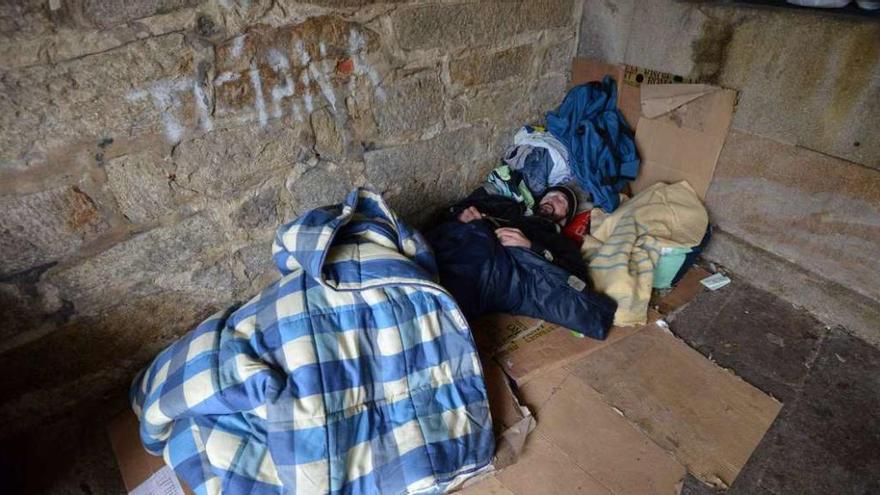Un hombre descansa en su cama fabricada con cartones, sacos de dormir y mantas en un soportal de A Ferrería. // Gustavo Santos