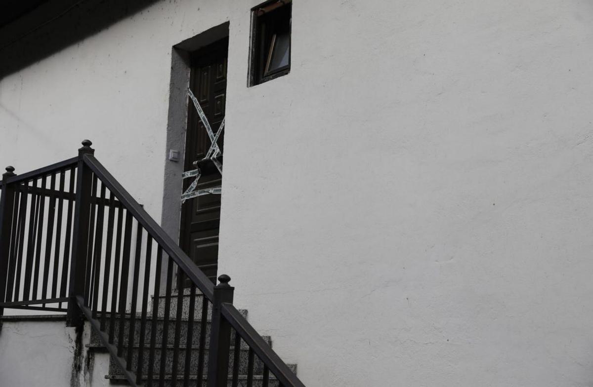 Arriba, vista panorámica de la vivienda donde vivían juntos el parricida y su padre; junto a estas líneas, las escaleras de acceso y la puerta de la vivienda, precintadas con cintas de la Guardia Civil. | Fernando Rodríguez
