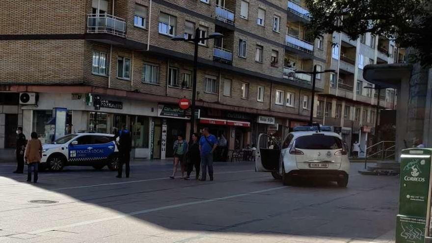 Despliegue policial, ayer por la tarde, en la plaza del Fresno (antigua Gesta), en Oviedo, con el hombre agredido, a la derecha, sentado junto a la iglesia redonda de la plaza y observando los coches policiales.