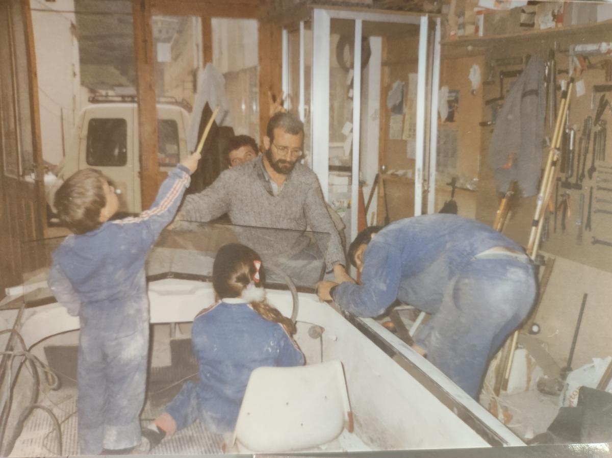 Camilo (en el centro) trabaja en la reparación de una lancha junto a dos empleados, mientras sus hijos juegan a bordo.