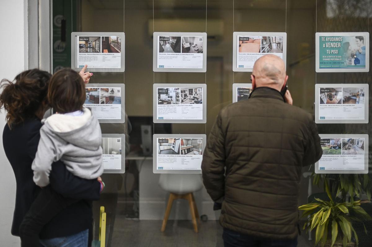 Dos personas miran los precios de alquiler y venta en el escaparate de una inmobiliaria.