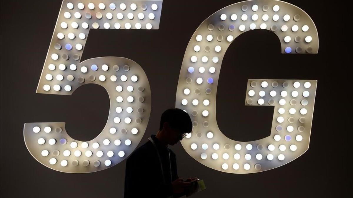 Un visitante usa su teléfono junto a un cartel de 5G en el estand de Intel