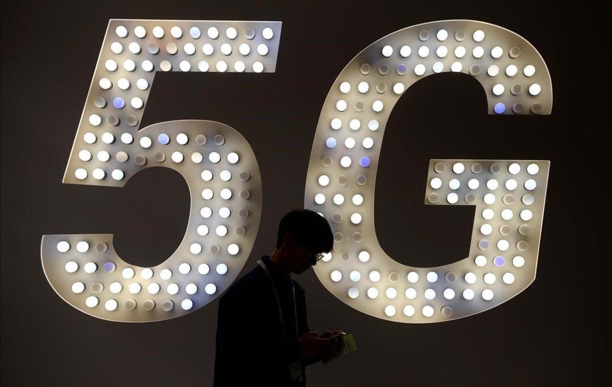 Un visitante usa su teléfono junto a un cartel de 5G.