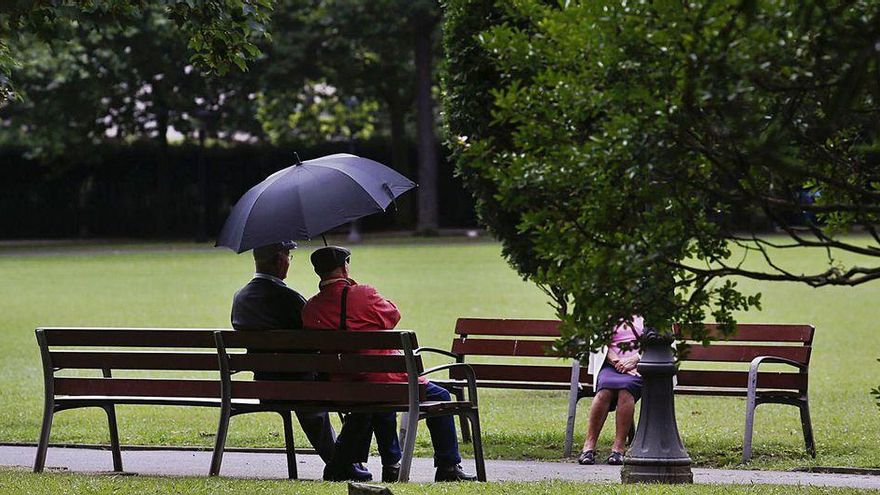 Ancianos conversando bajo un paraguas en el parque Ferrera.