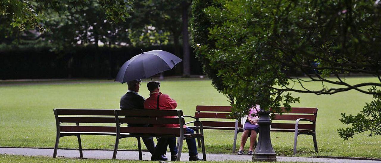 Ancianos conversando bajo un paraguas en el parque Ferrera.