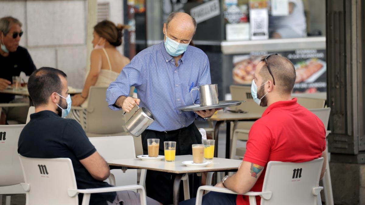 Los contagios por coronavirus siguen subiendo en España por encima del millar. En la foto, un camarero con mascarilla atiende a unos clientes en un bar de Madrid.
