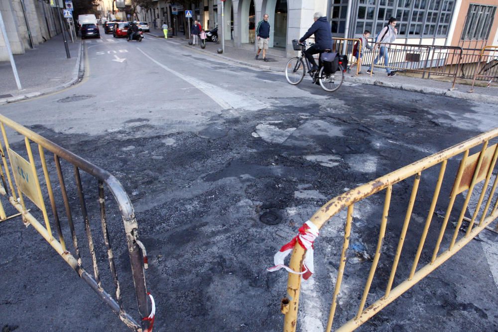 Carrers amb restes de mobiliari urbà cremat, contenidors per terra i treballadors de la brigada treballant