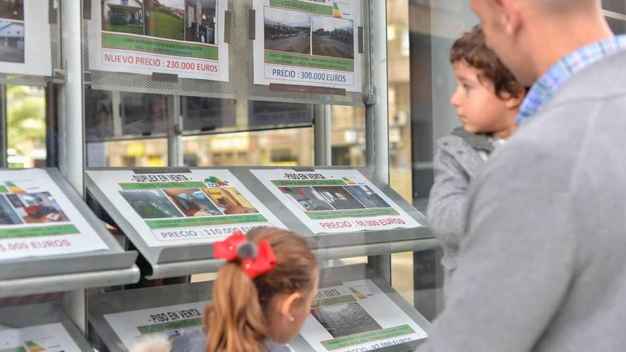 Un hombre con dos pequeños mira las ofertas inmobiliarias expuestas en el escaparate de una agencia avilesina.