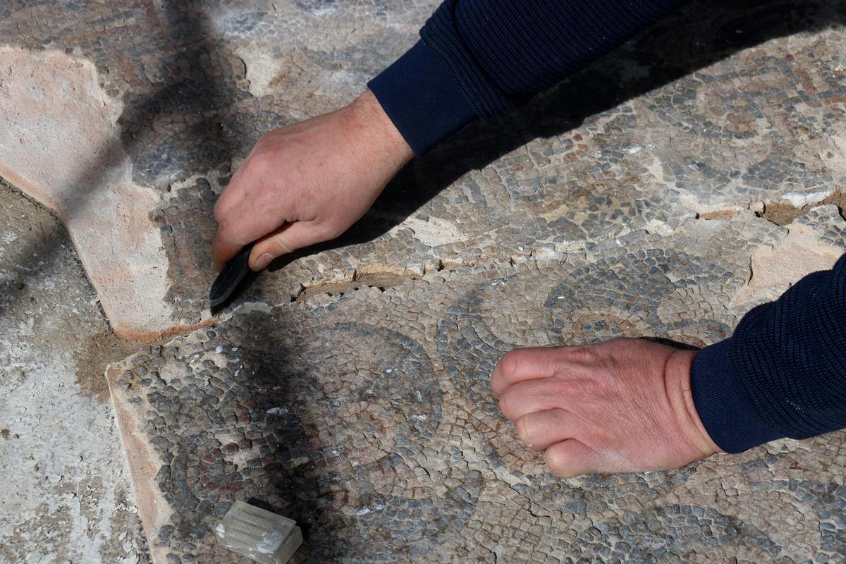 Detall de les mans d'un restaurador netejant la unió de dos fragments del mosaic romà
