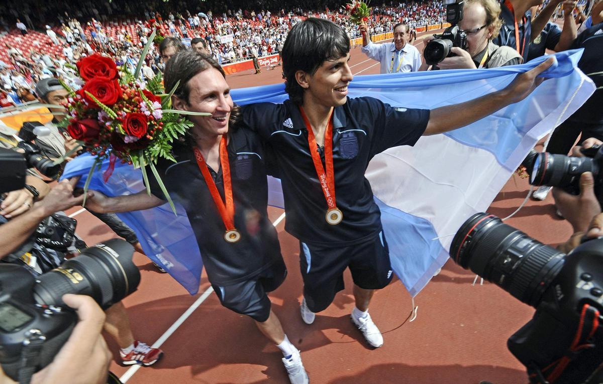 Los delanteros argentinos Lionel Messi (izq.) y Sergio Agüero, envueltos en la bandera nacional, posan durante la ceremonia de entrega de medallas del torneo olímpico de fútbol masculino. Los delanteros argentinos Lionel Messi (izq.) y Sergio Agüero, envueltos en la bandera nacional, posan durante la ceremonia de entrega de medallas del torneo olímpico de fútbol masculino.