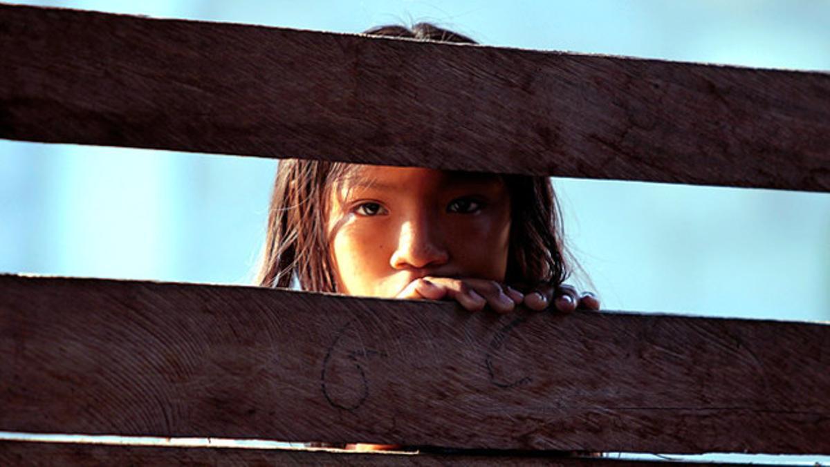 Una nena de la tribu Embera de Colòmbia mira a través de les taules de fusta de su casa.