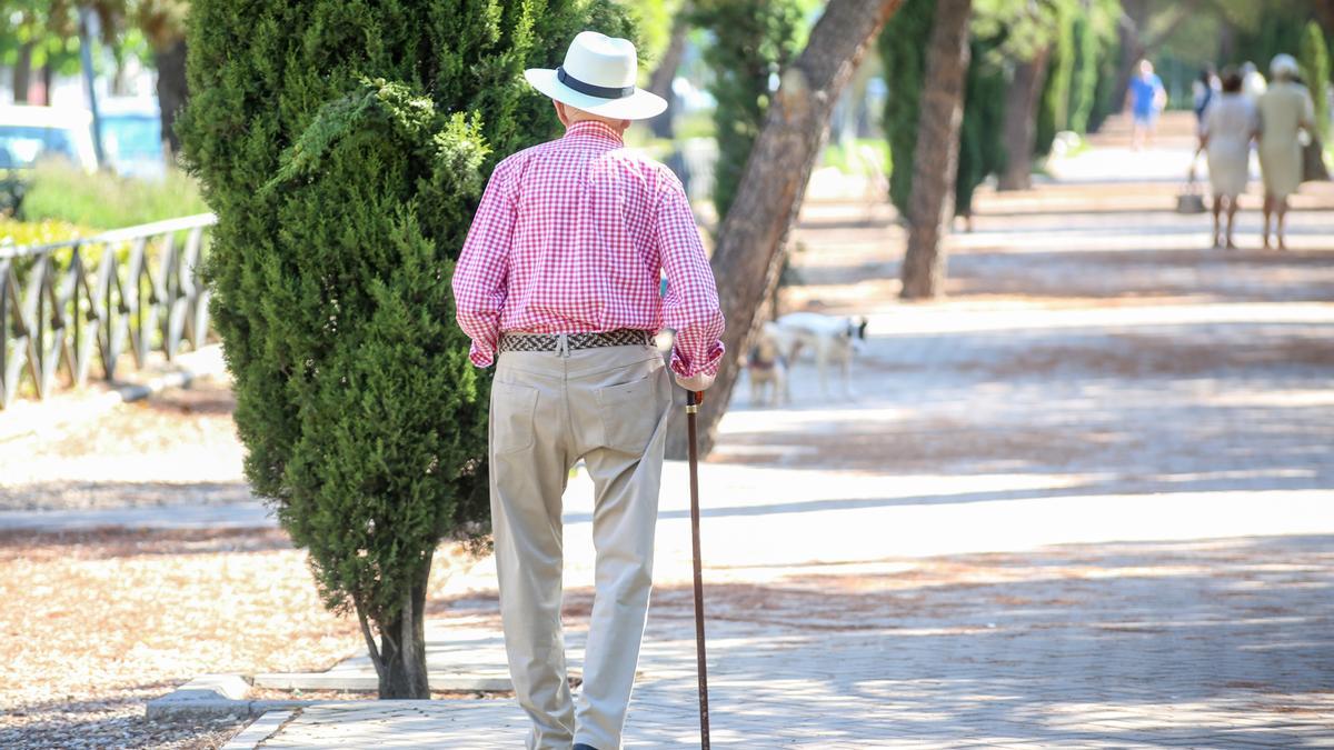 Un anciano pasea solo, apoyándose en su bastón.