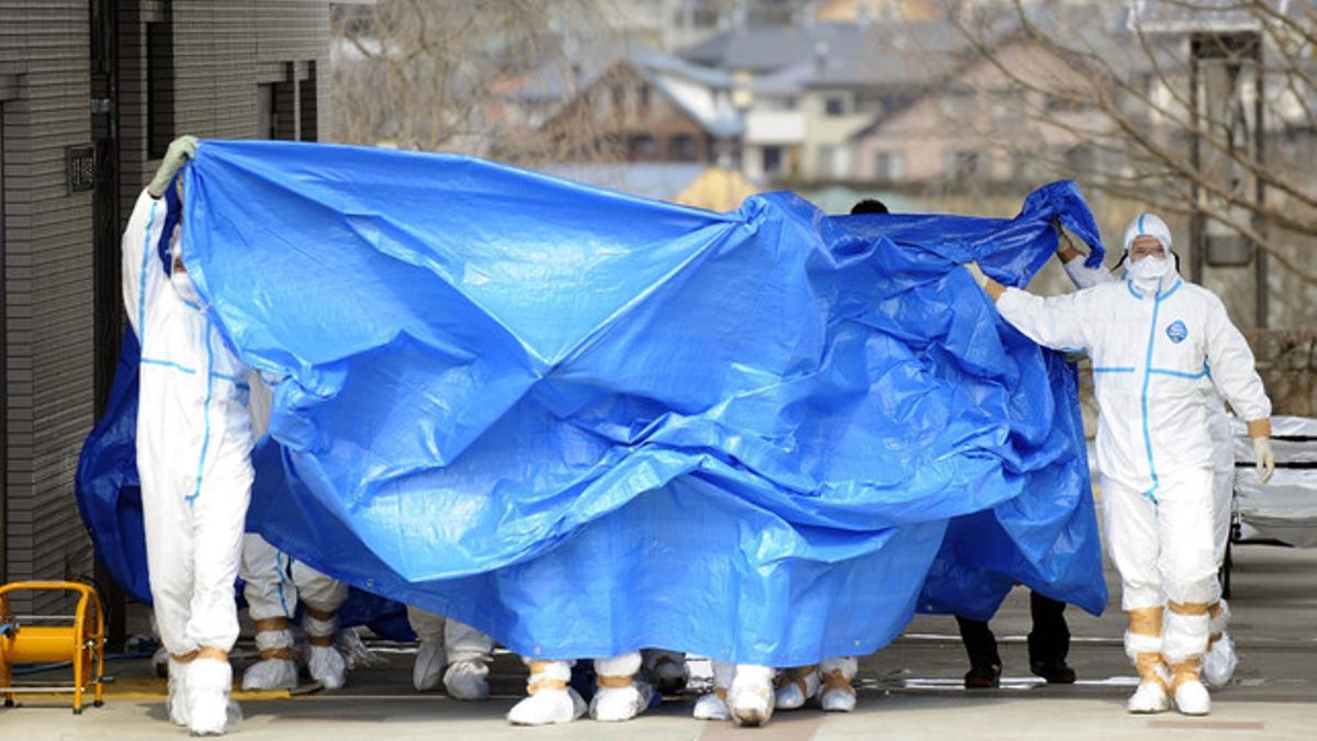 Trabajadores de la planta de Fukushima trasladan, cubiertos por una lona, a los dos operarios que pisaron agua contaminada, el jueves.