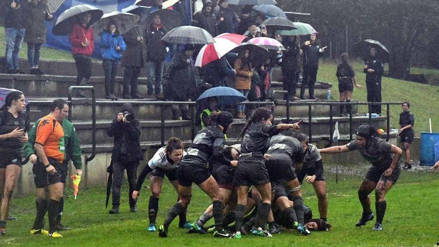 Las jugadoras, embarradas, y el público con paraguas en las gradas, en el CRAT-Hortaleza de ayer.