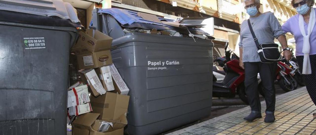 Dos señoras pasan junto a un contenedor de recogida de cartón y papel en Alicante