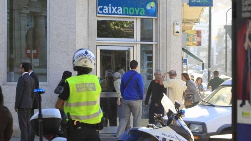 Agentes de la Policía Local y curiosos ante la sucursal de Novacaixagalicia en Bouzas. / r. grobas