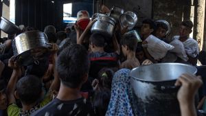 Cientos de palestinos desplazados se reúnen a las afueras del comedor benéfico Sokar en la ciudad de Gaza para recibir raciones limitadas de alimentos.
