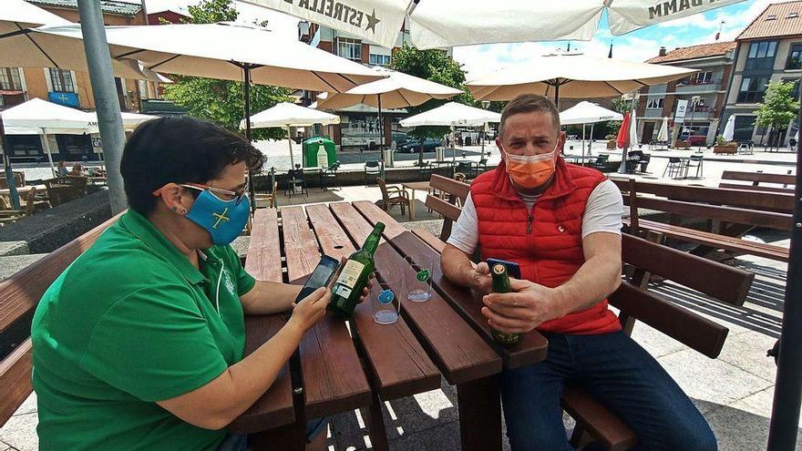 La hostelera Loreto García, enseñando ayer a su cliente Marco Antonio Álvarez cómo acceder a la información con el teléfono móvil en la plaza de Les Campes de Pola de Siero.