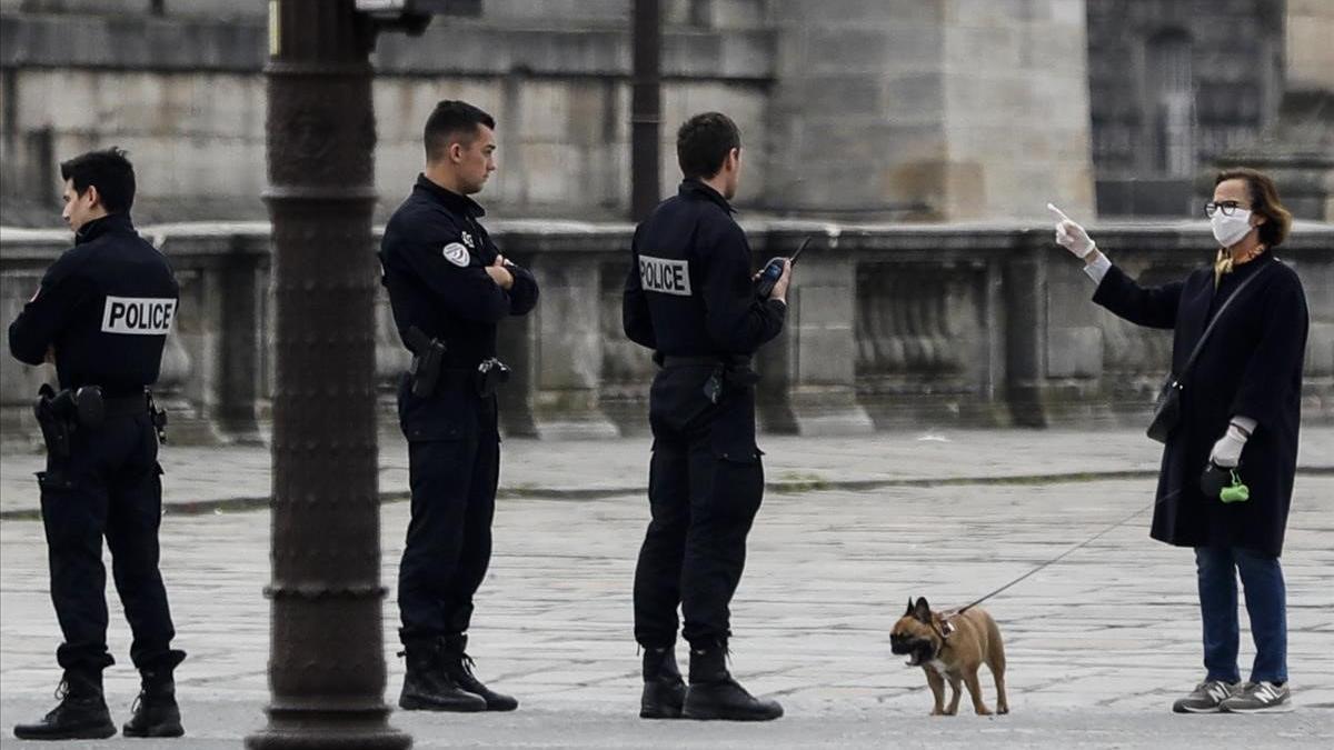 Unos gendarmes se dirigen a una mujer que pasea a su perro protegida con una máscara en la parisina plaza de la Concordia.