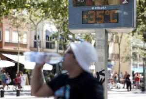 Un hombre bebe agua ante un termómetro que marca los 35 grados, en Barcelona.