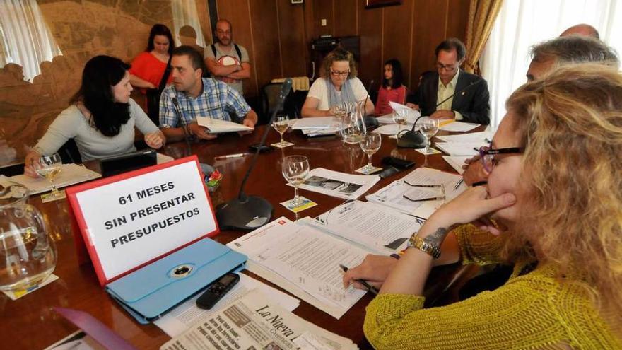 José Manuel Rodríguez, a la derecha, lee un documento durante el Pleno de Mieres de junio, con un cartel colocado por el PSOE que señala que el Ayuntamiento llevaba 61 meses sin presupuestos.