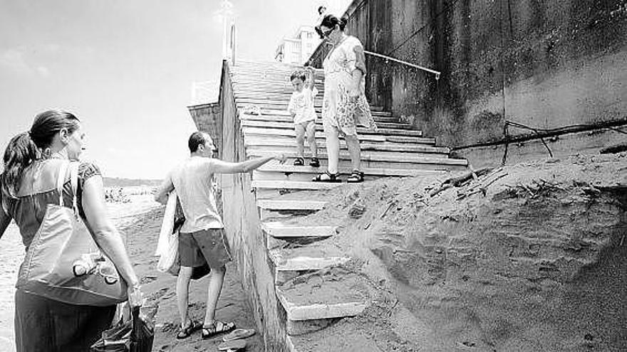 Una familia, ayer, en una de las escaleras de la playa, tapada por un metro de arena, a la altura de los «Gauzones».