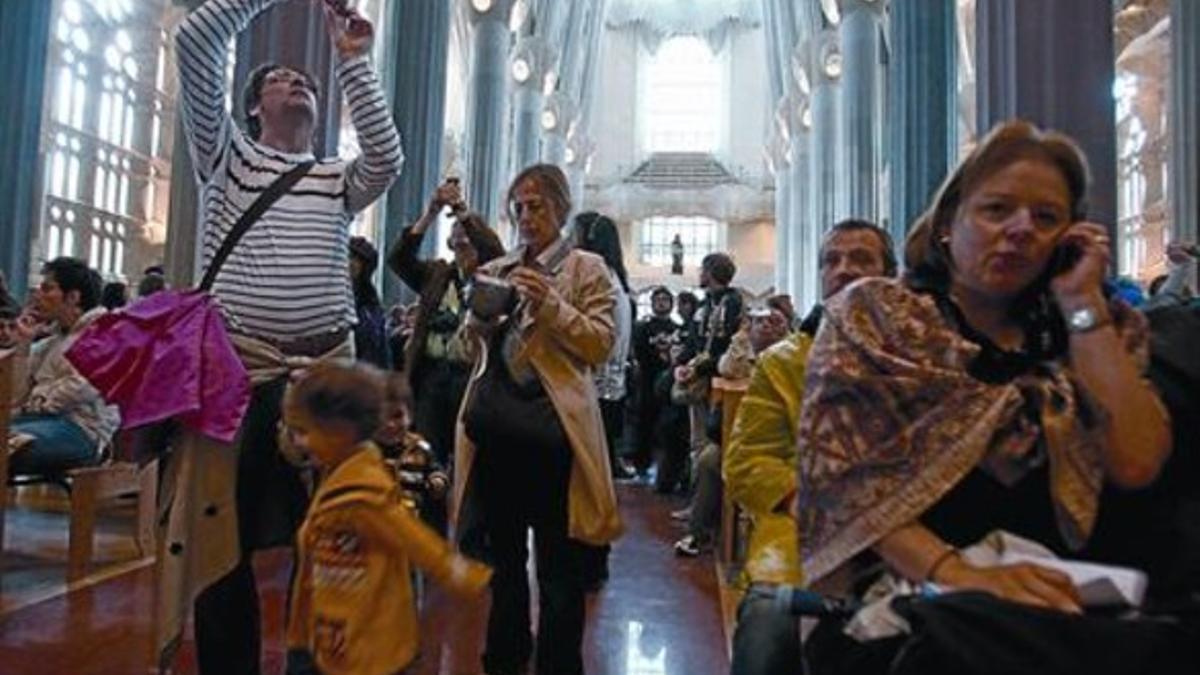 Una mujer habla por el móvil rodeada de turistas que sacan partido de sus cámaras y niños que corren por la Sagrada Família, ayer por la mañana.