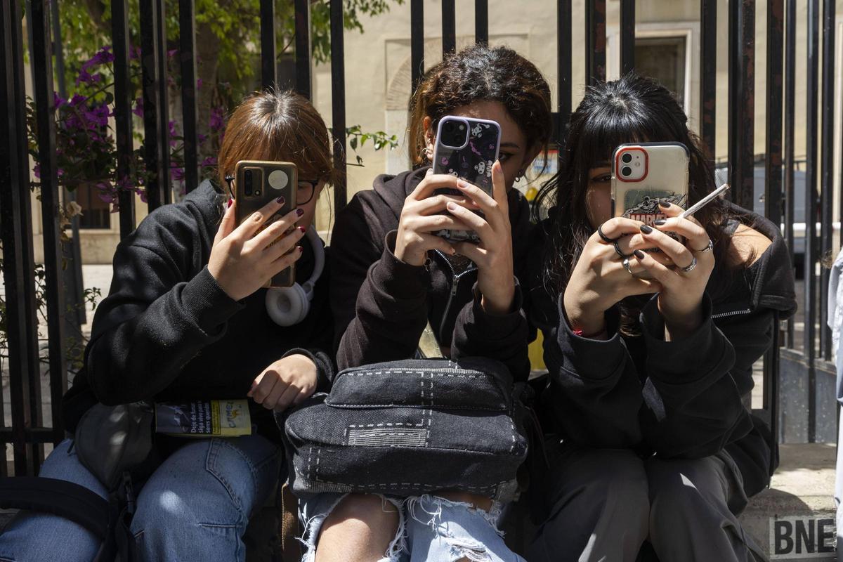 Varias jóvenes con su teléfono móvil en la puerta de un IES de València.