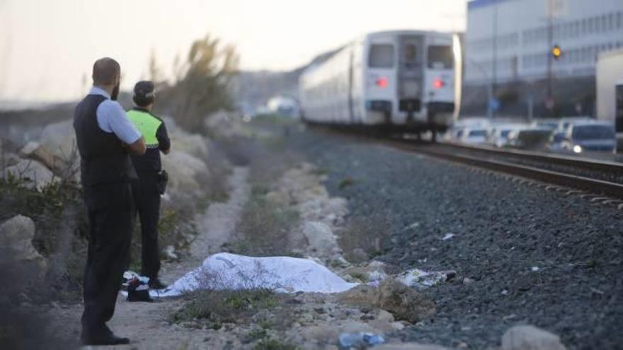 Un policía local junto al cuerpo tapado de la mujer atropellada y al fondo el tren detenido tras el accidente.