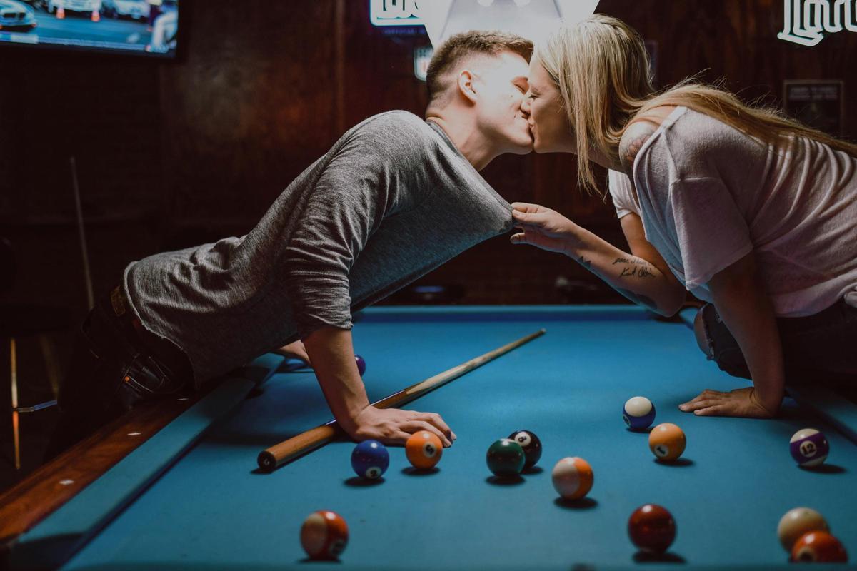 Una pareja se besa mientras juega al billar.