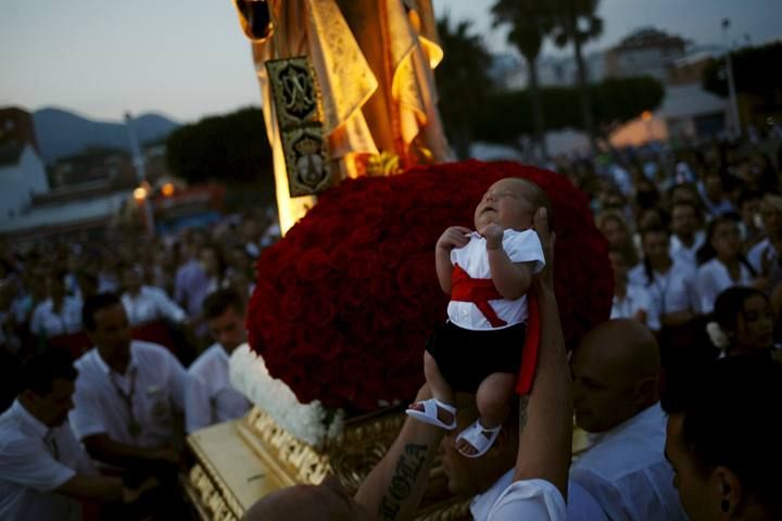 A man holds a child as they take part in the procession of the El Carmen Virgin being carried into the sea in Malaga
