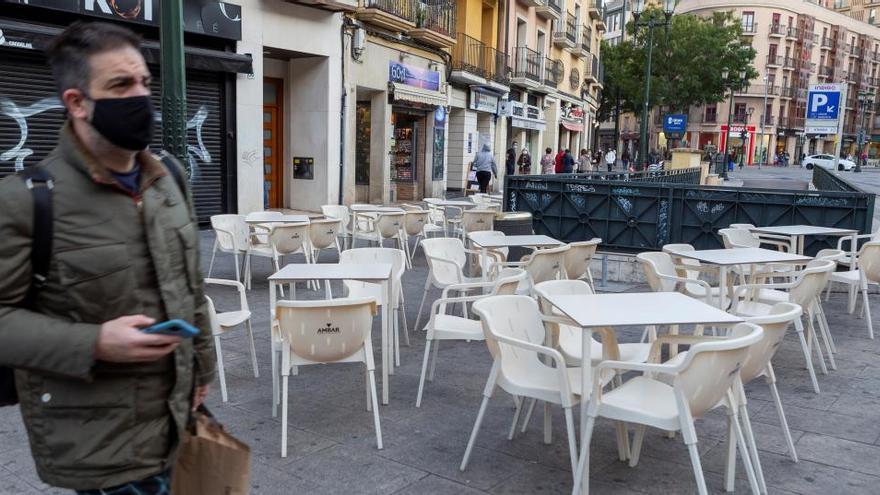 Un hombre camina junto a una terraza vacía en Zaragoza.