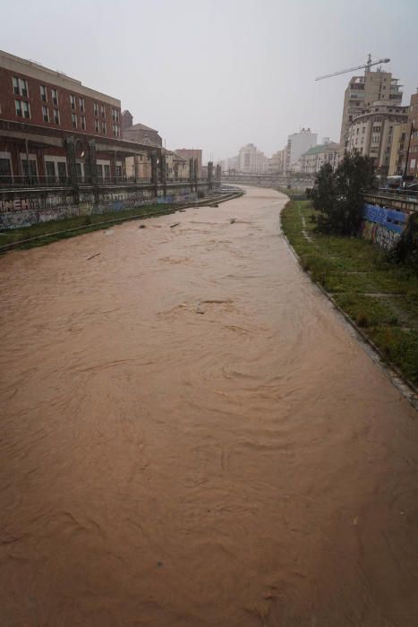 El río Guadalmedina crecido con agua y calles del Centro y el entorno del cauce, desiertas bajo la lluvia, la estampa de este martes 31 de marzo.