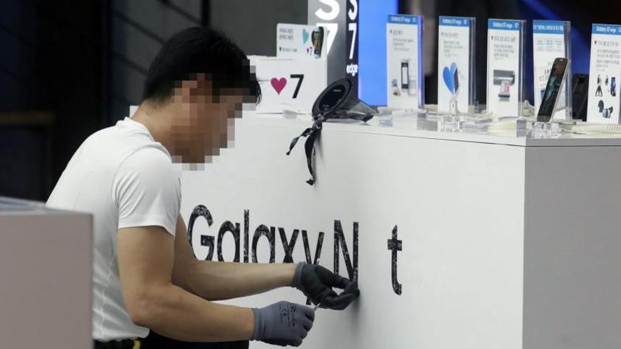 Un treballador retira la marca publicitària del model Galaxy Note 7 de Samsung en una botiga de Seül