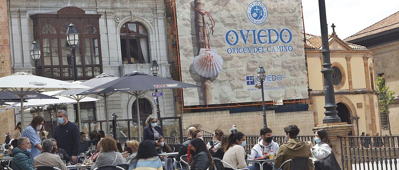 Terrazas hosteleras llenas, ayer, con la lona promocional de “Oviedo, origen del Camino”, de fondo. | Miki López