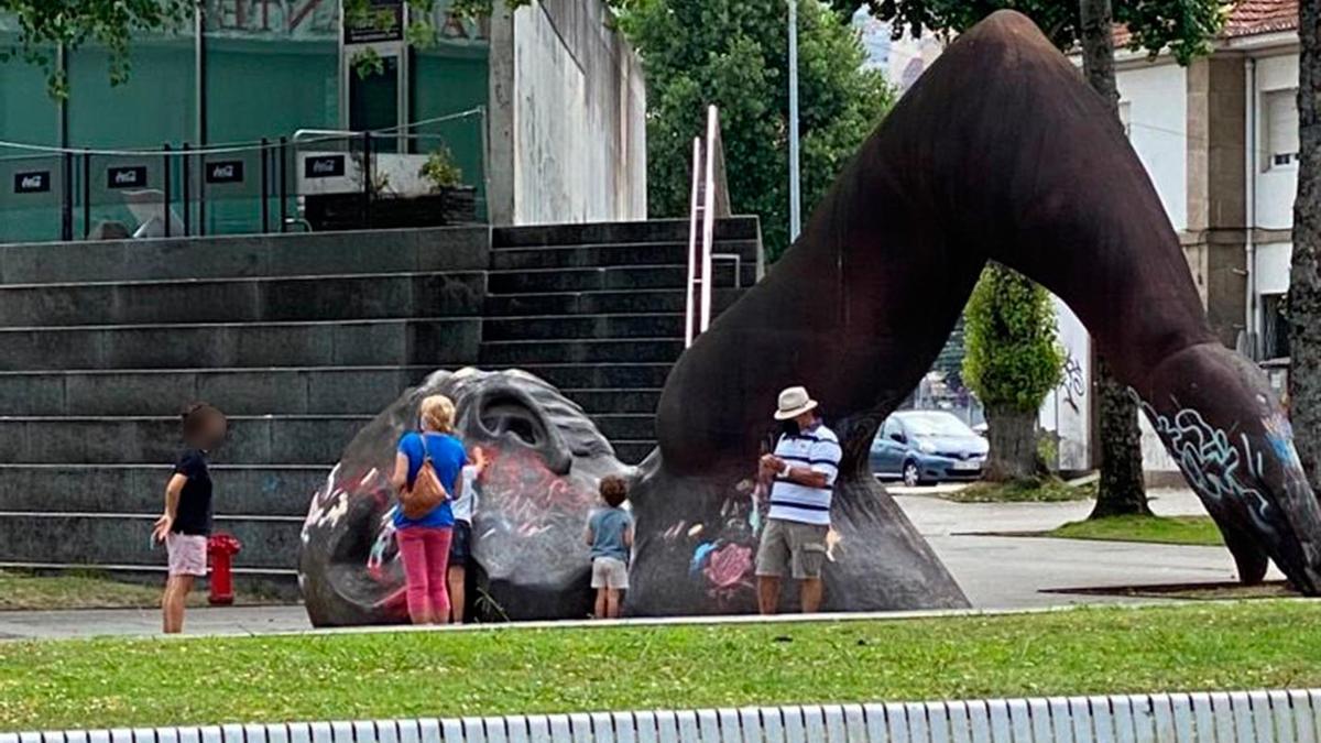Dos niños pintarrajean la estatua de El Nadador ante la atenta mirada de sus padres