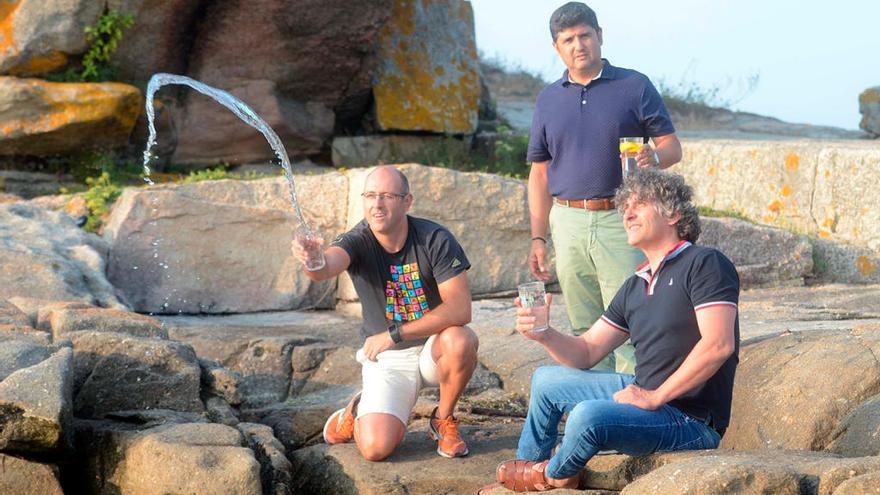 Pablo Dosil lanzando un vaso de agua de mar, con Juan Luis Boo a su espalda y Juan Ramón Arines sentado en Punta Cabalo. // Noé Parga