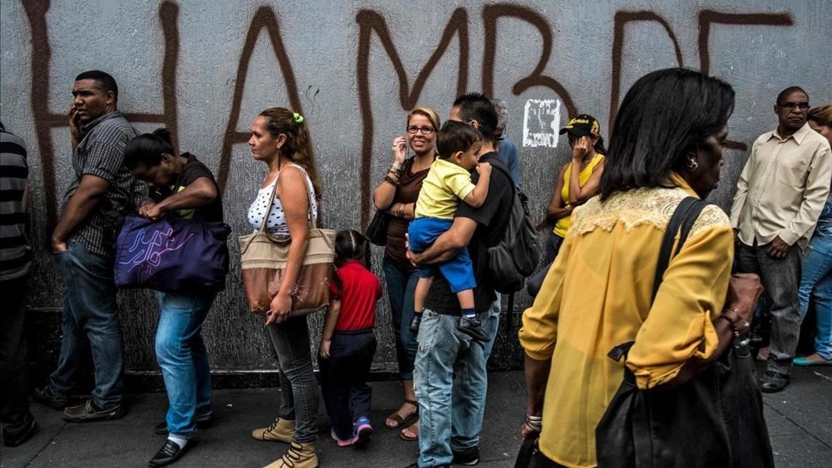 Venezolanos hacen cola frente a una pintada con la palabra 'hambre', en Caracas.
