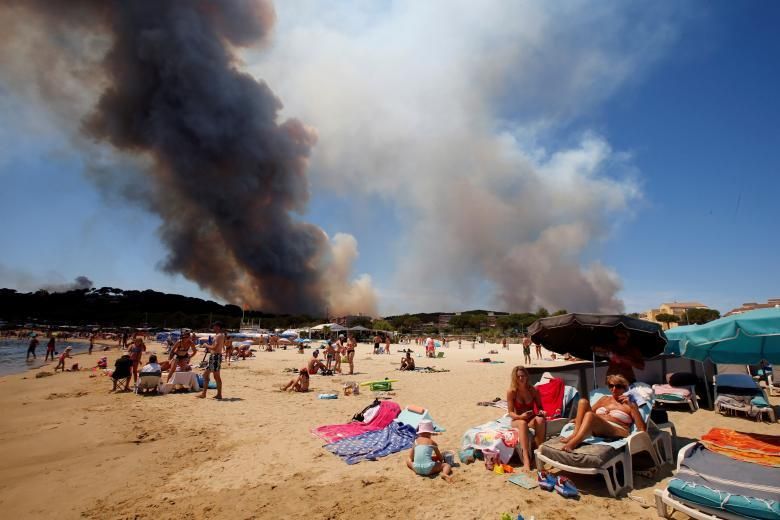 El fum frega el cel per sobre d'un turó cremant a mesura que els turistes es relaxen a la platja al departament francès de Var, el 26 de juliol.