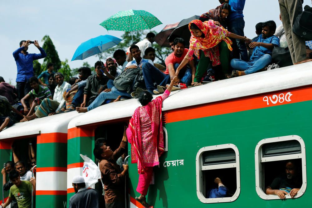 Una mujer ayuda a otra a subir a lo alto de un tren de pasajeros repleto de personas que acuden a celebrar el festival de Eid al-Fitr en una estación de ferrocarril en Dhaka, Bangladesh.