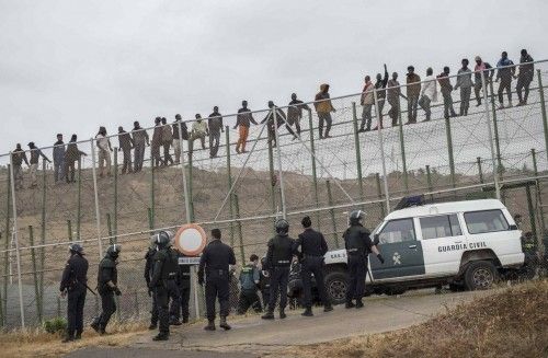 African migrants climb a border fence, as Spanish Civil Guard officers stand under them, during a latest attempt to cross into Spanish territory, between Morocco and Spain's north African enclave of Melilla