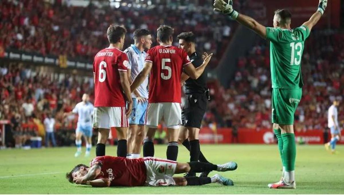 El árbitro del Nástic - Málaga CF rodeado de jugadores